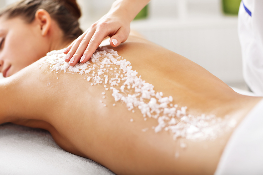 A woman receives a body exfoliation massage as salt is rubbed into her back.