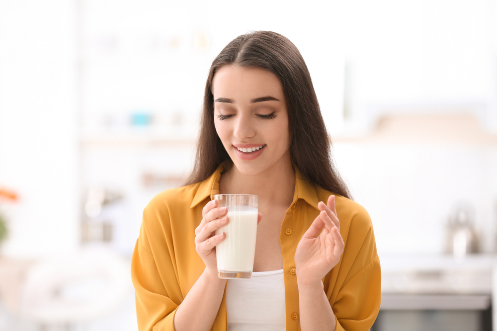 A young woman smiles as she picks up a glass of milk.