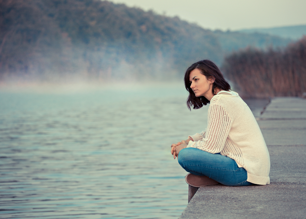 Woman sits on a dock thinking by the water