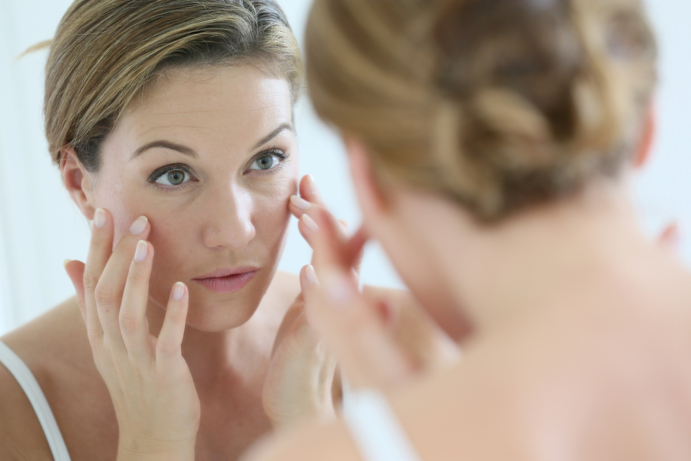 A young woman looks in the mirror and applies a skin cream.