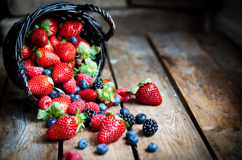Mix of fresh berries in a basket on rustic wooden background
