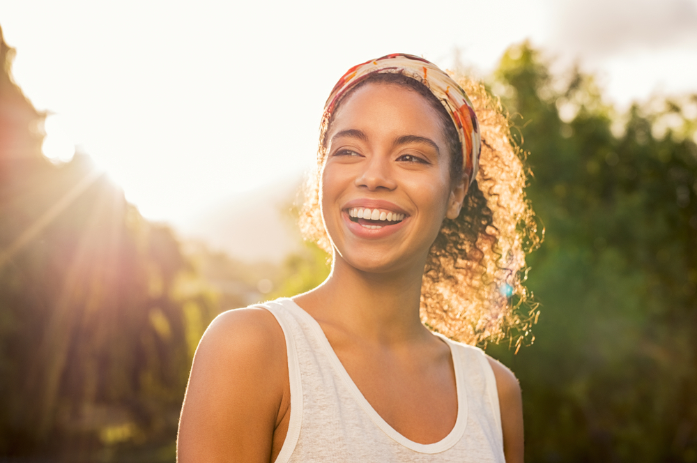A smiling woman stands in the sunlight reaping the benefits of the sun.