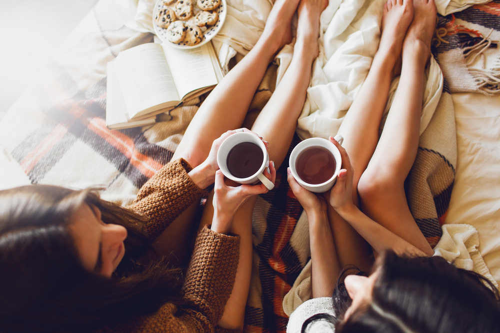 Soft photo of two sisters on the bed with old books and cup of tea in hands wearing cozy sweater , top view point. Two best friends enjoying morning.