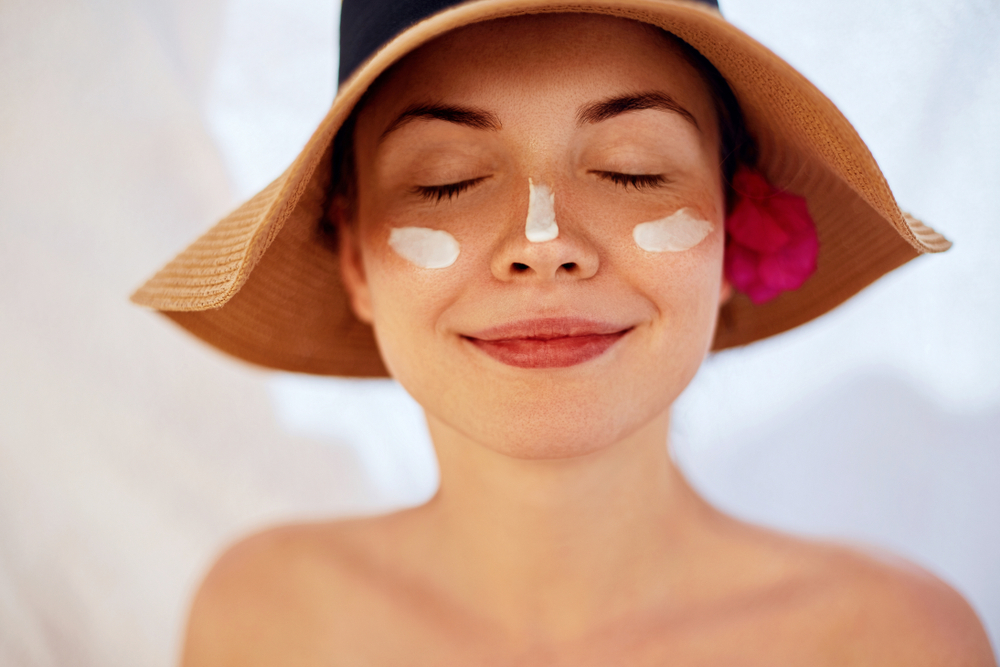 Smiling woman in a hat with sunscreen on her face.