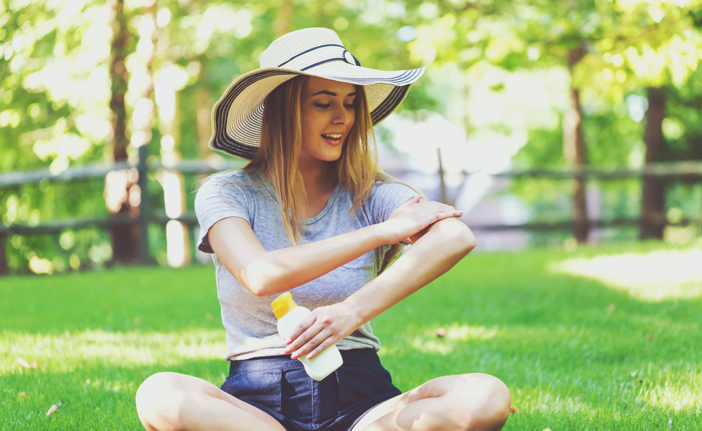 Woman sitting outside in protective hat, applying sunscreen